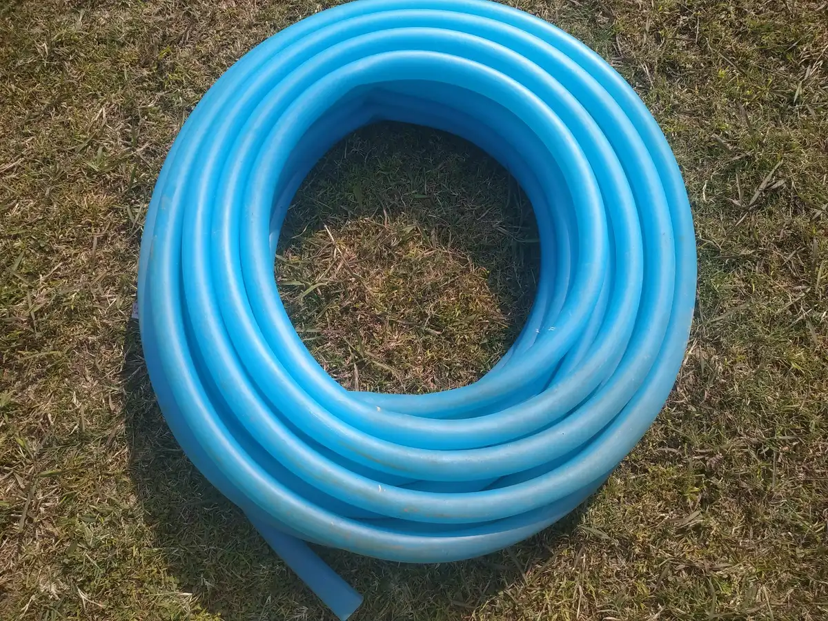 A coiled light blue garden hose lying on dry grass