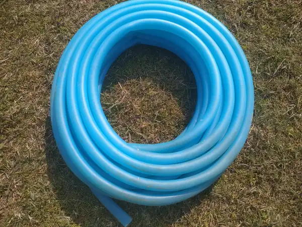A coiled light blue garden hose lying on dry grass
