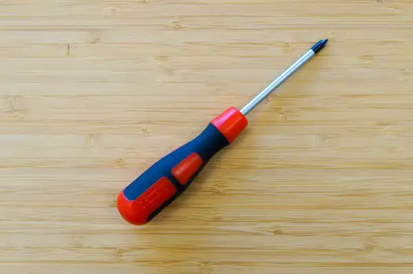 A red and blue screwdriver lying on a pale bamboo workbench